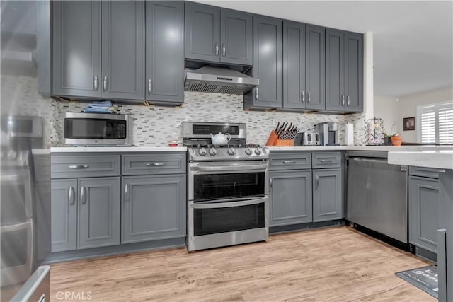 kitchen with tasteful backsplash, appliances with stainless steel finishes, gray cabinets, range hood, and light hardwood / wood-style floors