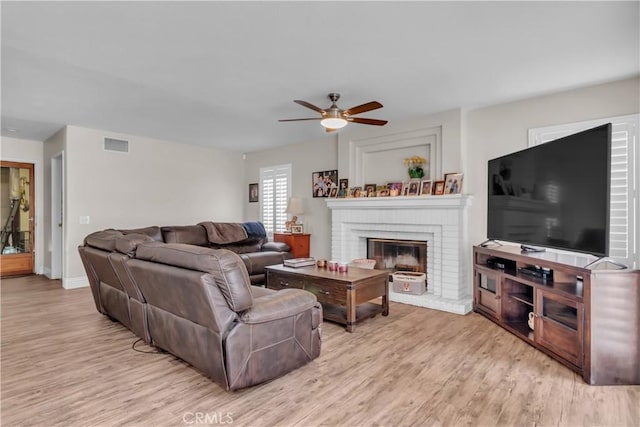 living room featuring ceiling fan, a brick fireplace, and light wood-type flooring