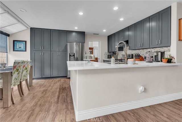 kitchen featuring gray cabinetry, light hardwood / wood-style floors, stainless steel fridge with ice dispenser, decorative backsplash, and kitchen peninsula