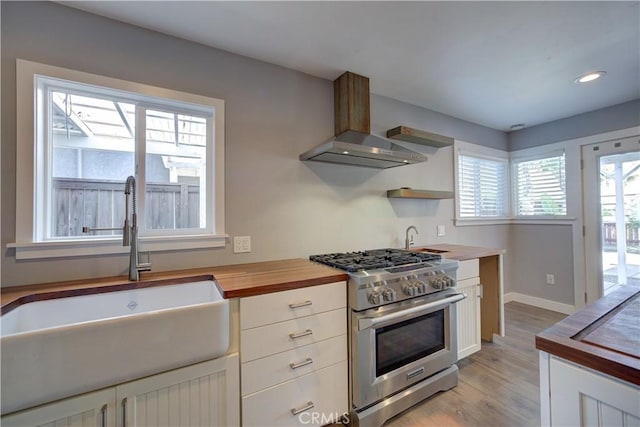 kitchen with white cabinetry, wooden counters, a sink, high end range, and wall chimney exhaust hood