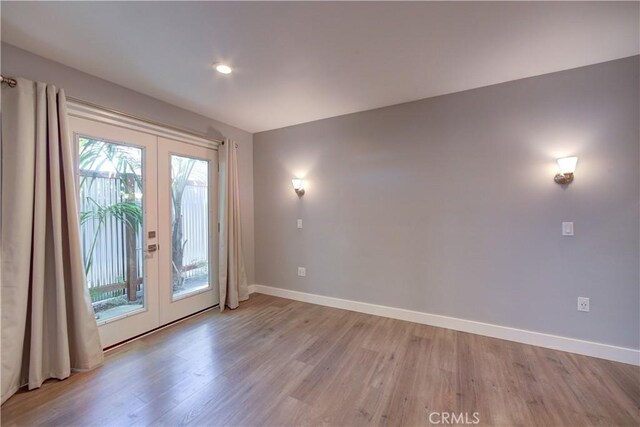 spare room with baseboards, light wood-style flooring, and french doors