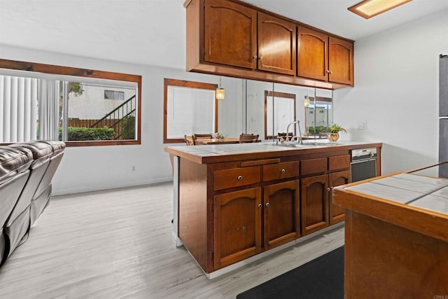 kitchen with tile countertops, kitchen peninsula, sink, and light hardwood / wood-style flooring