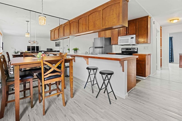 kitchen featuring hanging light fixtures, light hardwood / wood-style flooring, stainless steel appliances, and a breakfast bar area