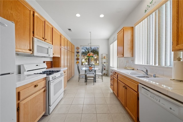 kitchen with sink, white appliances, light tile patterned floors, tile counters, and decorative light fixtures