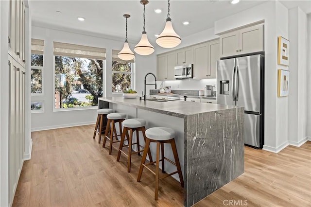 1090 Foothill Blvd, Claremont, CA 91711 - kitchen with appliances with stainless steel finishes, a kitchen island with sink, a kitchen bar, light wood finished floors, and recessed lighting