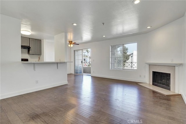 unfurnished living room featuring recessed lighting, dark wood-style flooring, a fireplace, a ceiling fan, and baseboards