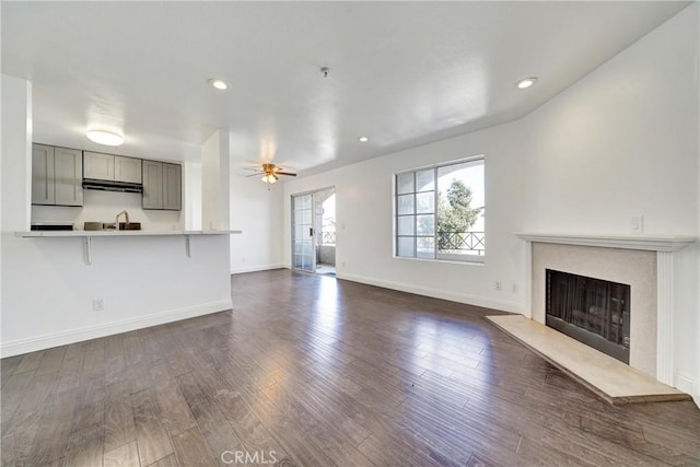 unfurnished living room with recessed lighting, a fireplace with raised hearth, dark wood-type flooring, a ceiling fan, and baseboards