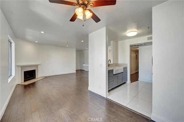 unfurnished living room featuring light wood finished floors, a fireplace, baseboards, and a sink