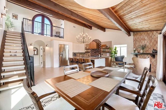 tiled dining room with sink, wood ceiling, a notable chandelier, beam ceiling, and a high ceiling