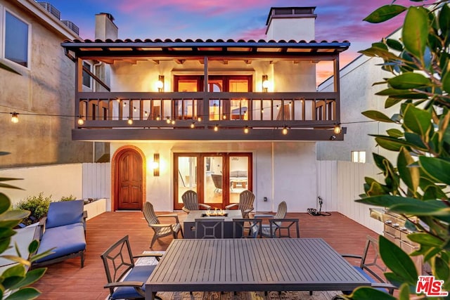 back house at dusk with a balcony and an outdoor fire pit