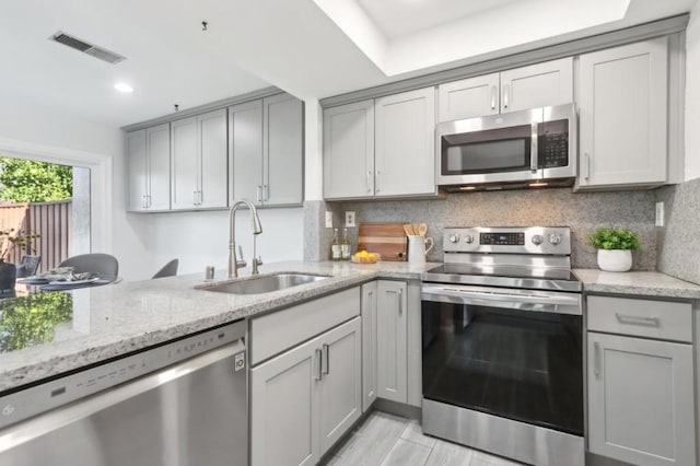 kitchen featuring appliances with stainless steel finishes, sink, gray cabinetry, and light stone counters