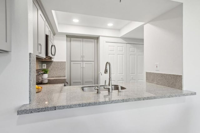 kitchen with light stone countertops, sink, kitchen peninsula, and a tray ceiling