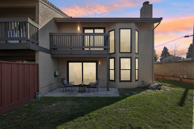 back house at dusk with a balcony, a yard, and a patio