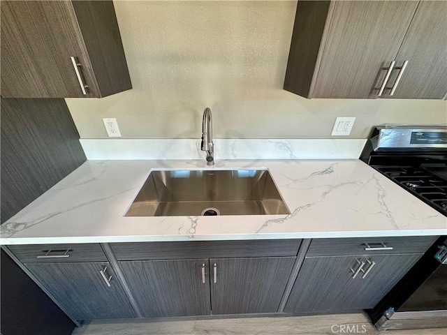 kitchen featuring gas stove, light stone countertops, and sink