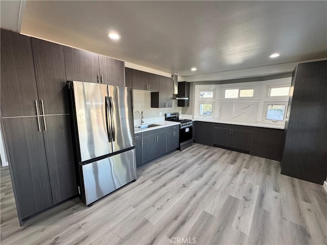 kitchen featuring sink, dark brown cabinetry, stainless steel appliances, wall chimney range hood, and light hardwood / wood-style flooring