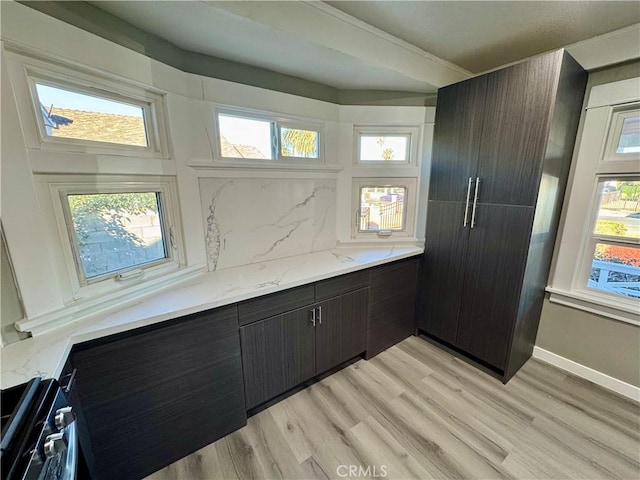 kitchen featuring stainless steel stove, light hardwood / wood-style flooring, dark brown cabinetry, tasteful backsplash, and light stone countertops