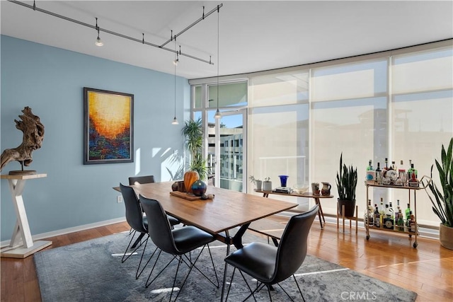 dining area with hardwood / wood-style flooring, a wall of windows, and rail lighting