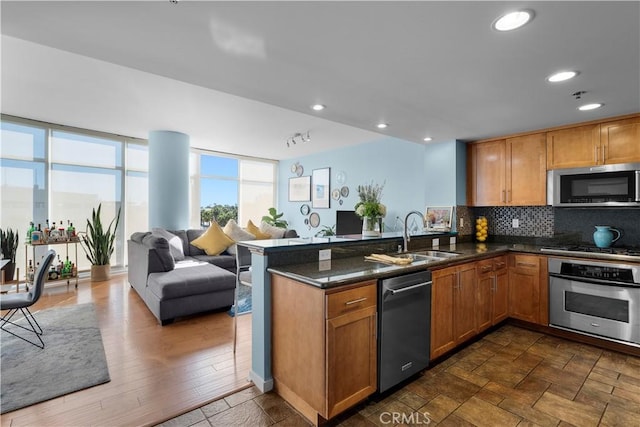 kitchen with sink, appliances with stainless steel finishes, dark stone countertops, decorative backsplash, and kitchen peninsula