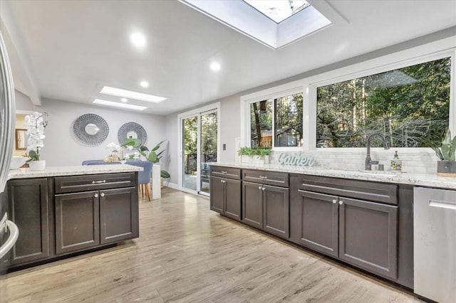 kitchen with a skylight, sink, light stone counters, dark brown cabinetry, and light hardwood / wood-style flooring