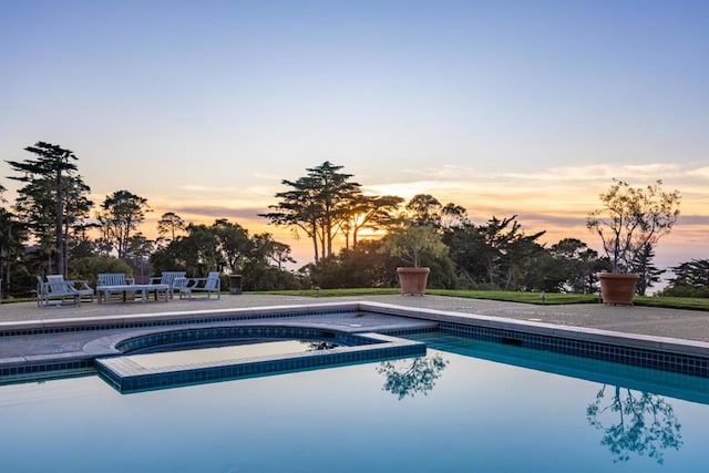 pool at dusk featuring a patio and an in ground hot tub