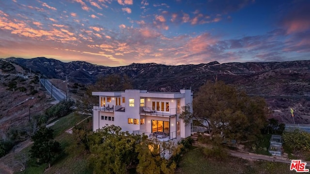 back house at dusk with a mountain view and a balcony