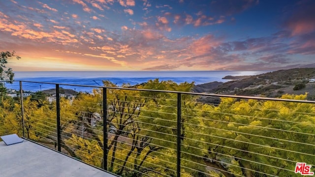 balcony at dusk featuring a water view