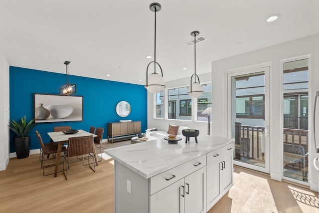 kitchen with pendant lighting, white cabinetry, a center island, light stone countertops, and light hardwood / wood-style flooring