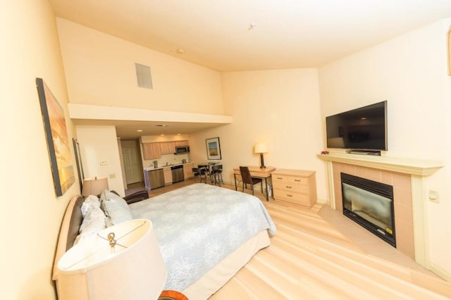 bedroom featuring a tiled fireplace, high vaulted ceiling, and light wood-type flooring