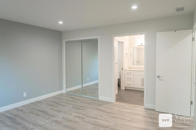 unfurnished bedroom featuring connected bathroom, light hardwood / wood-style floors, and a closet