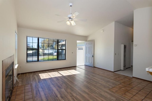 unfurnished living room with lofted ceiling, a tiled fireplace, wood-type flooring, and ceiling fan