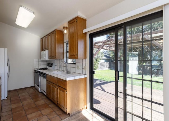 kitchen with sink, white appliances, dark tile patterned floors, backsplash, and tile counters