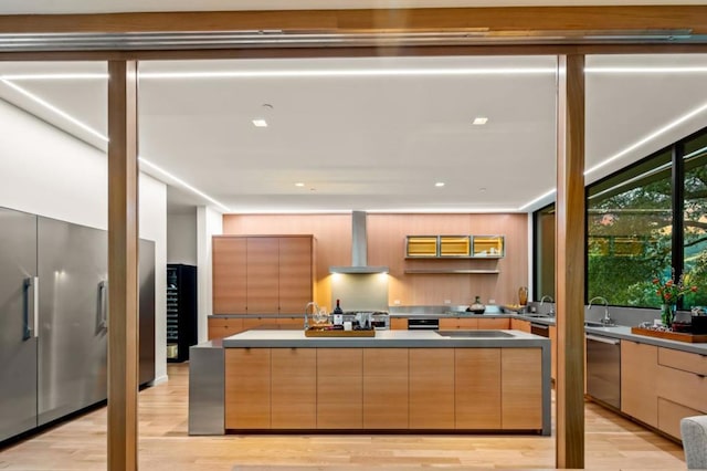 kitchen with stainless steel dishwasher, wall chimney exhaust hood, light brown cabinetry, and light wood-type flooring