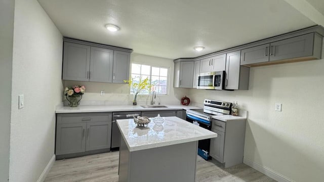 kitchen with sink, gray cabinets, stainless steel appliances, a center island, and light hardwood / wood-style floors