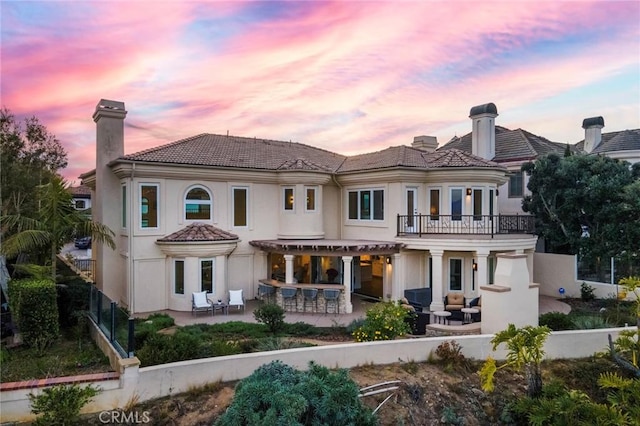 back house at dusk with a balcony and a patio area