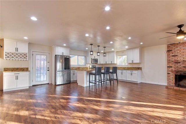 kitchen featuring stainless steel appliances, a center island, a kitchen breakfast bar, white cabinets, and decorative light fixtures