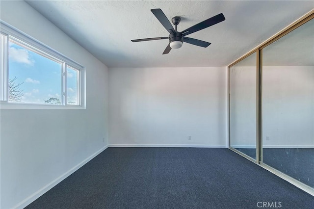 spare room with ceiling fan and dark colored carpet