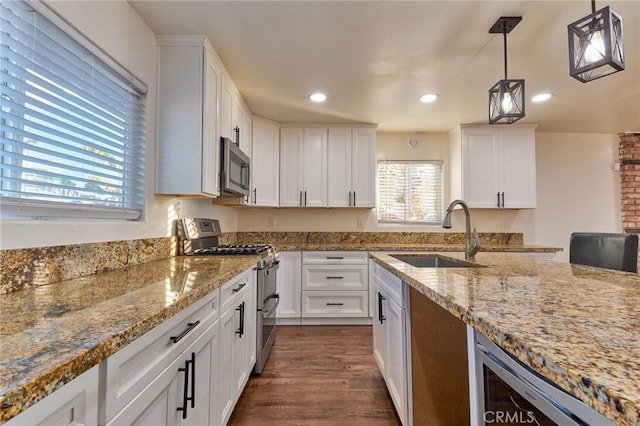 kitchen with appliances with stainless steel finishes, pendant lighting, white cabinetry, sink, and light stone counters