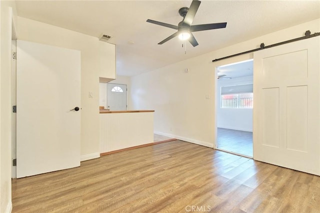 spare room with ceiling fan, a barn door, and light hardwood / wood-style floors