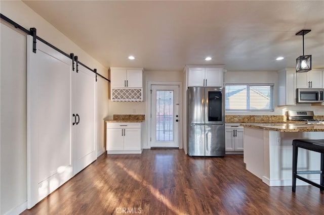 kitchen featuring appliances with stainless steel finishes, white cabinetry, a kitchen breakfast bar, decorative light fixtures, and a barn door