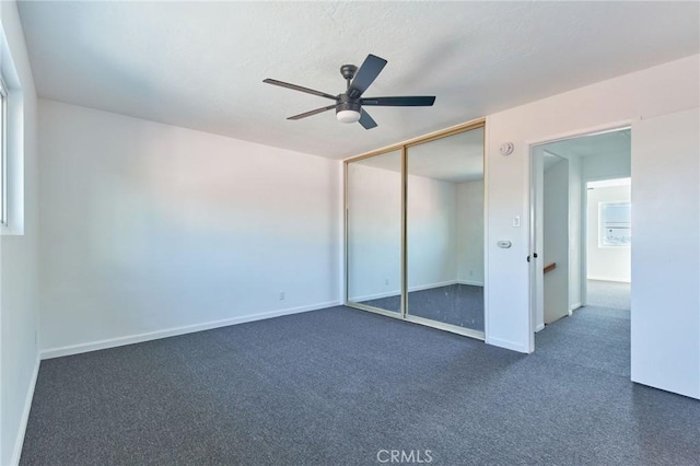 unfurnished bedroom with dark colored carpet, ceiling fan, and a closet