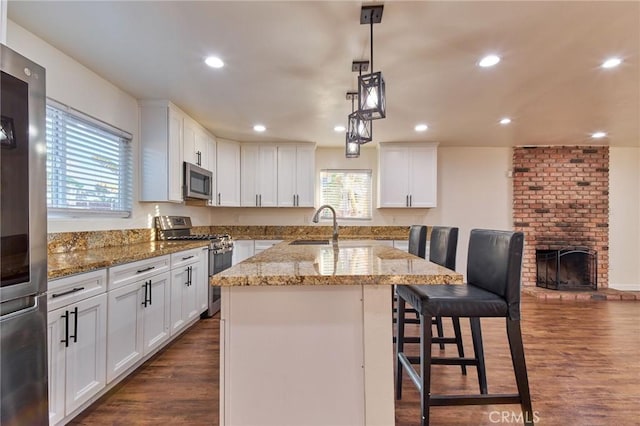 kitchen with stainless steel appliances, a kitchen island with sink, white cabinets, and a kitchen breakfast bar