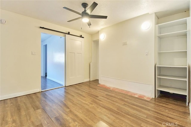 unfurnished room featuring hardwood / wood-style floors, a barn door, and ceiling fan