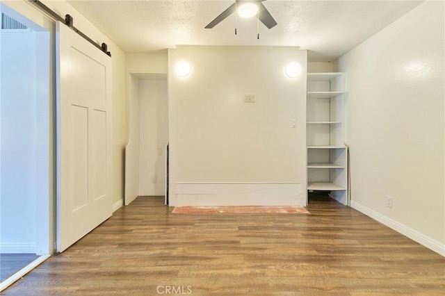 unfurnished bedroom featuring a textured ceiling, wood-type flooring, a barn door, and ceiling fan