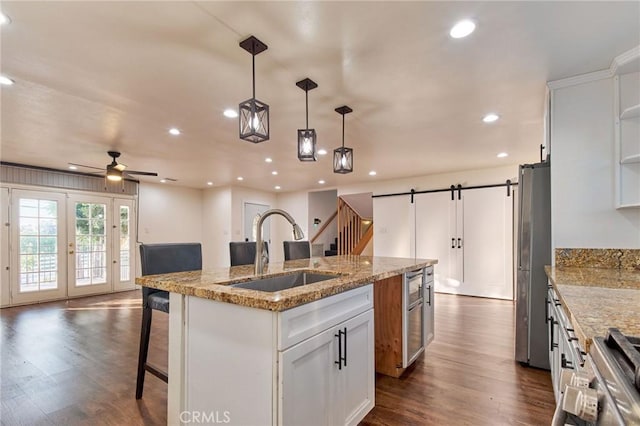 kitchen featuring sink, stainless steel refrigerator, white cabinetry, a kitchen island with sink, and a barn door