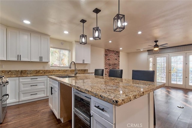 kitchen with white cabinetry, sink, beverage cooler, and a center island with sink