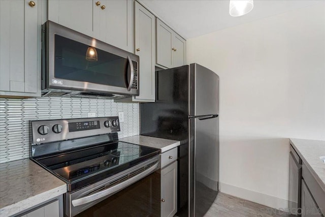 kitchen with gray cabinetry, backsplash, light hardwood / wood-style flooring, and appliances with stainless steel finishes