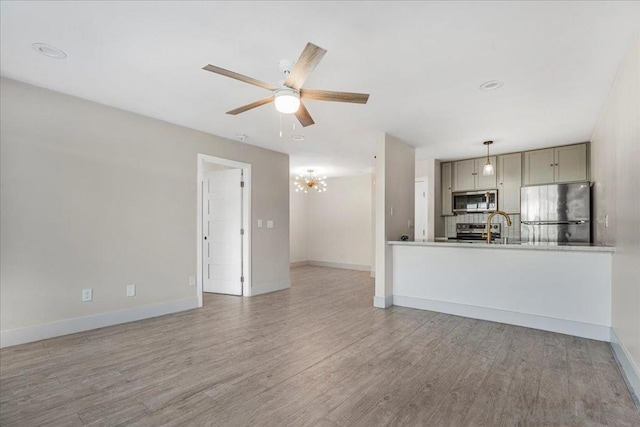 unfurnished living room with sink, ceiling fan with notable chandelier, and light hardwood / wood-style flooring