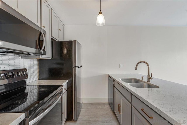 kitchen featuring sink, appliances with stainless steel finishes, hanging light fixtures, tasteful backsplash, and light stone countertops