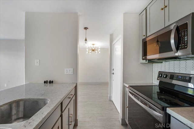 kitchen featuring gray cabinetry, light stone counters, appliances with stainless steel finishes, pendant lighting, and light hardwood / wood-style floors