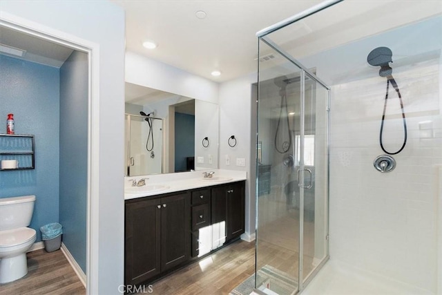 bathroom with toilet, a stall shower, a sink, and wood finished floors